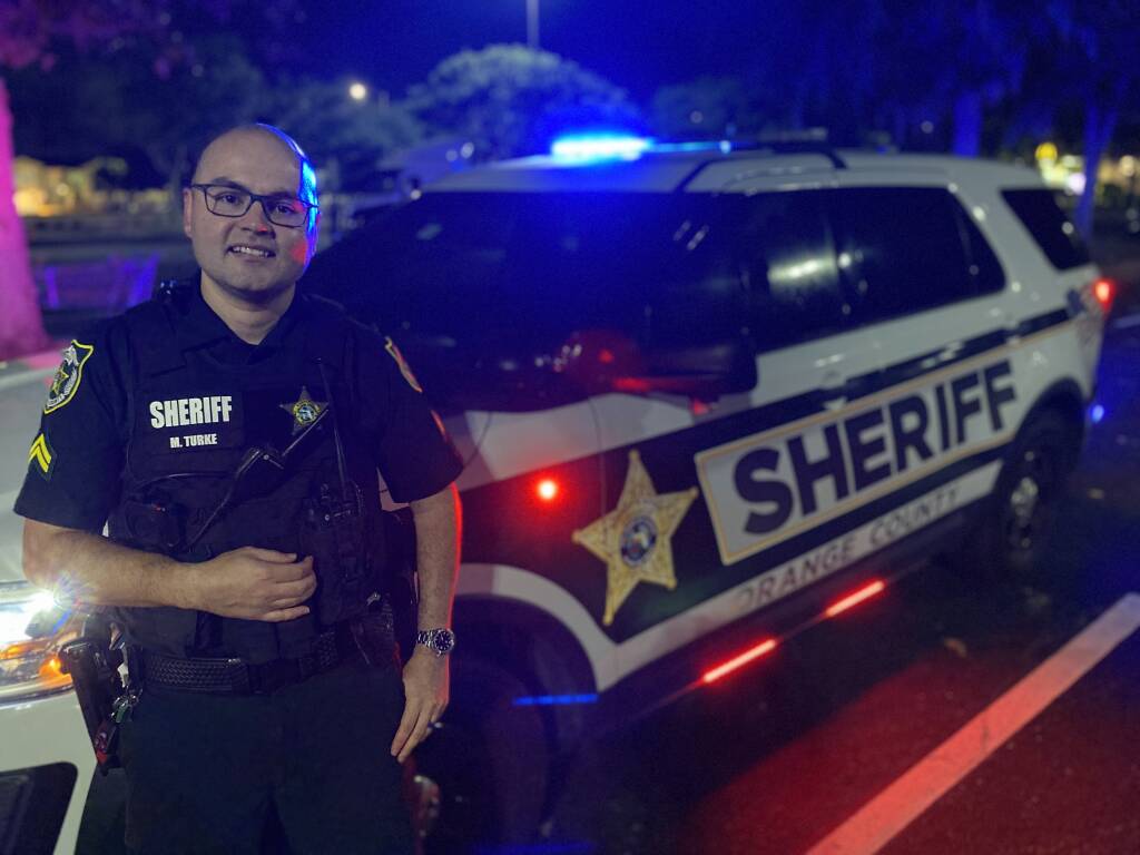 A deputy posing in front of his car with the lights on