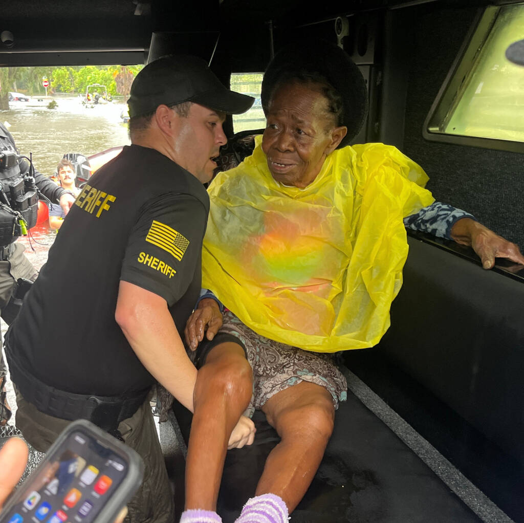 Deputy carrying an elderly woman into a Sheriff's office vehicle in a flooded neighborhood